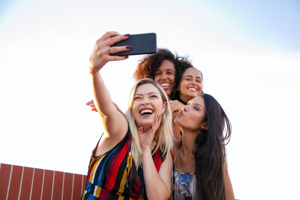 Instagram context, four women taking selfie on cell phone