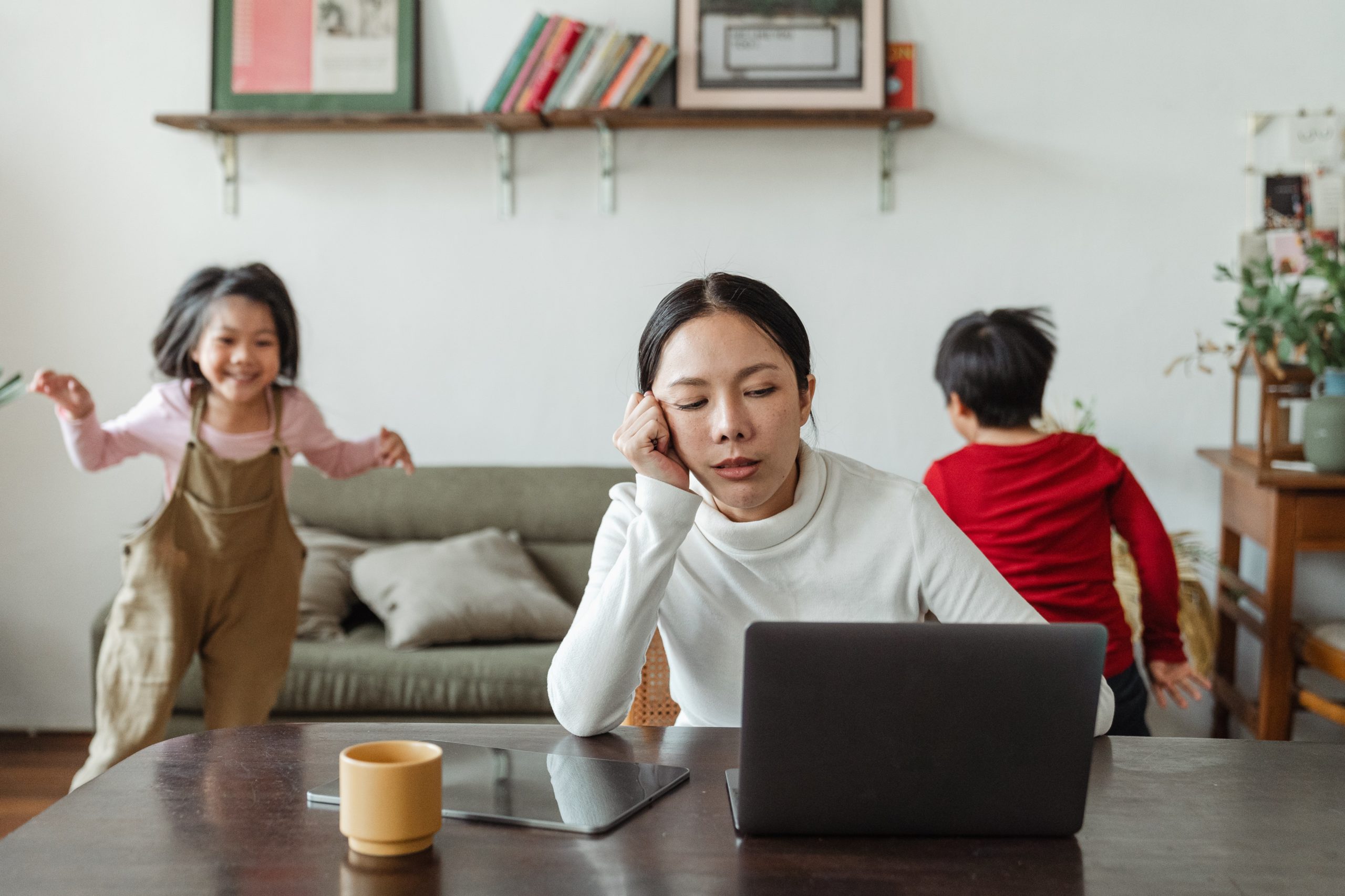 Mother at laptop overwhelmed by noisy, wild children in background