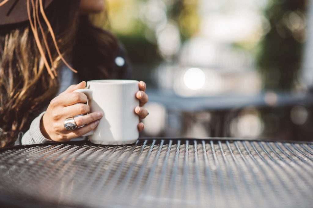 Chronic illness context, woman sitting at cafe table with coffee cup