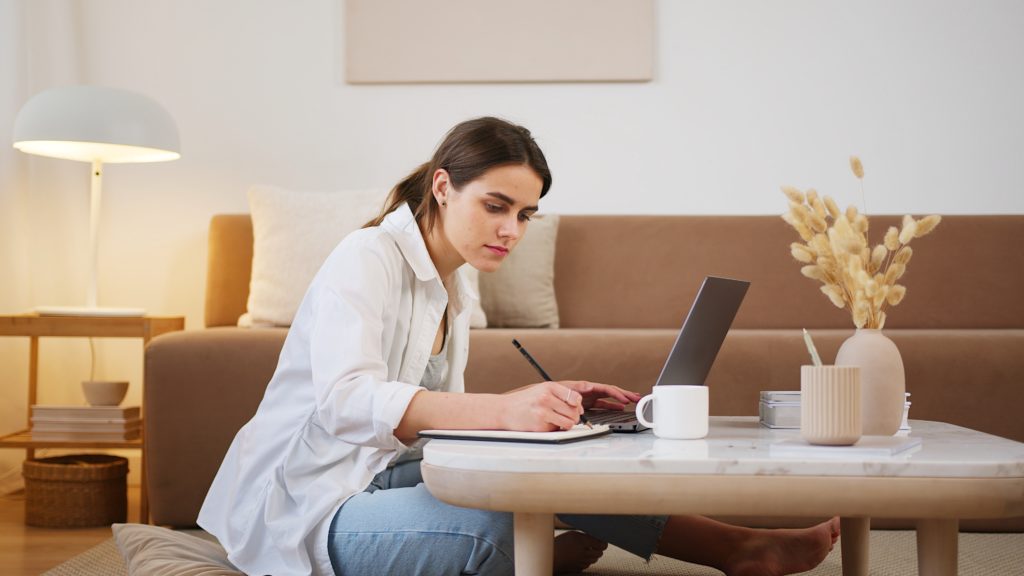 Brand voice context, woman sitting in front of laptop writing in notebook