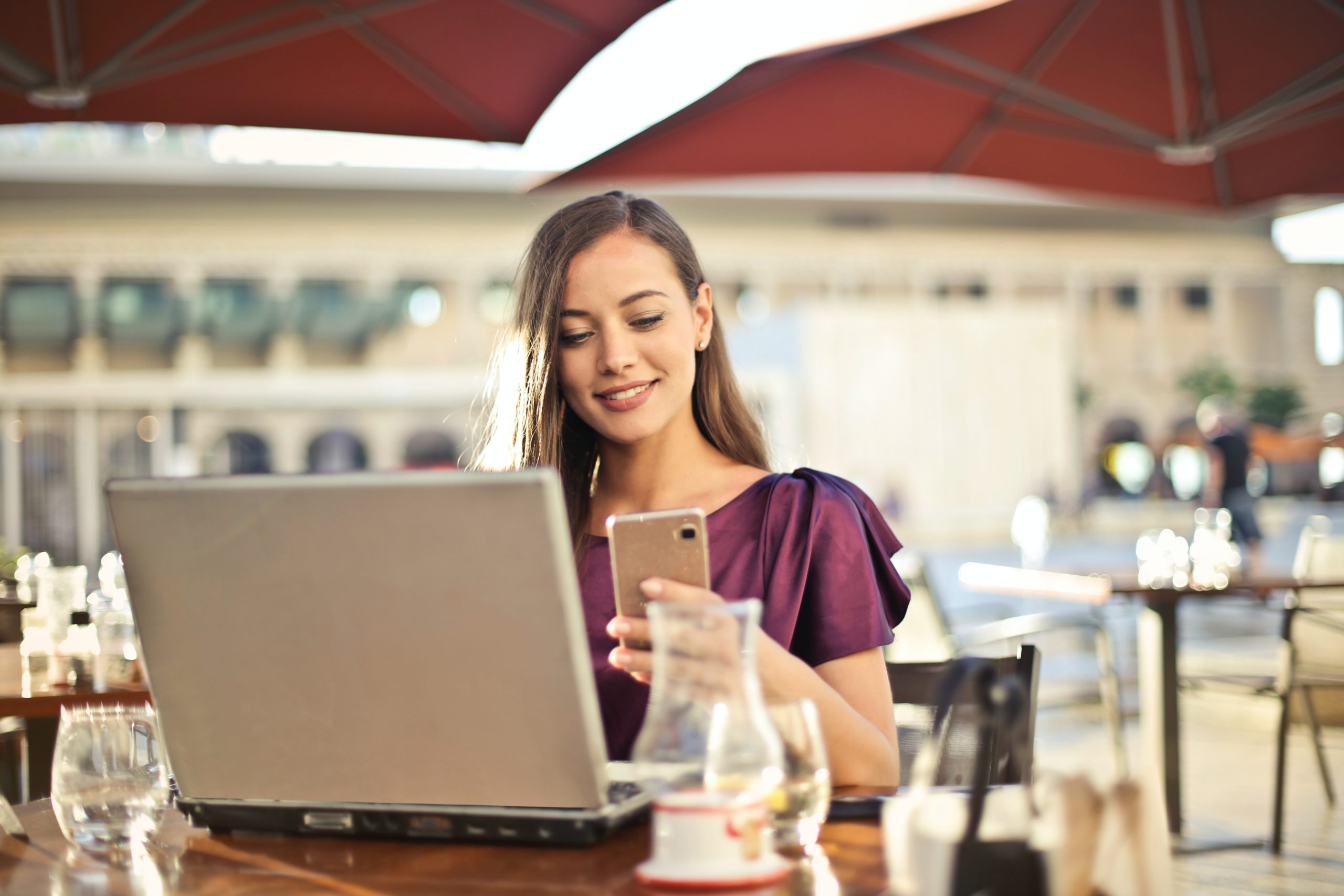 Online business context, woman sitting at table with laptop and cell phone