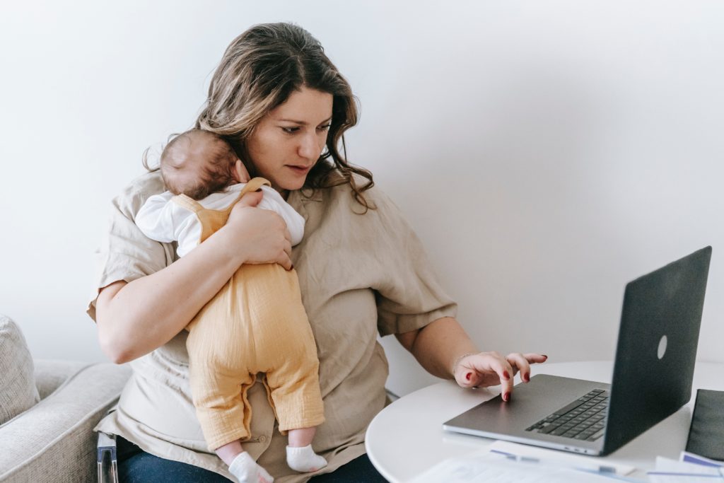 CEO context, mom with baby in arms sitting at table on laptop